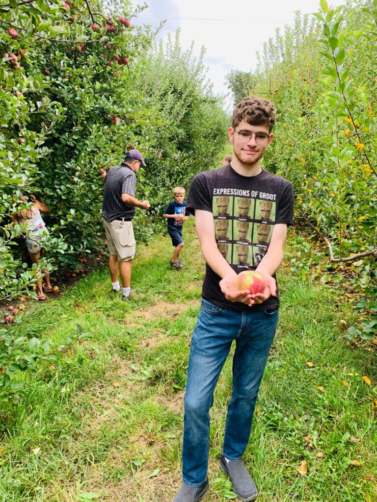 autistic teen boy picking apples with his family